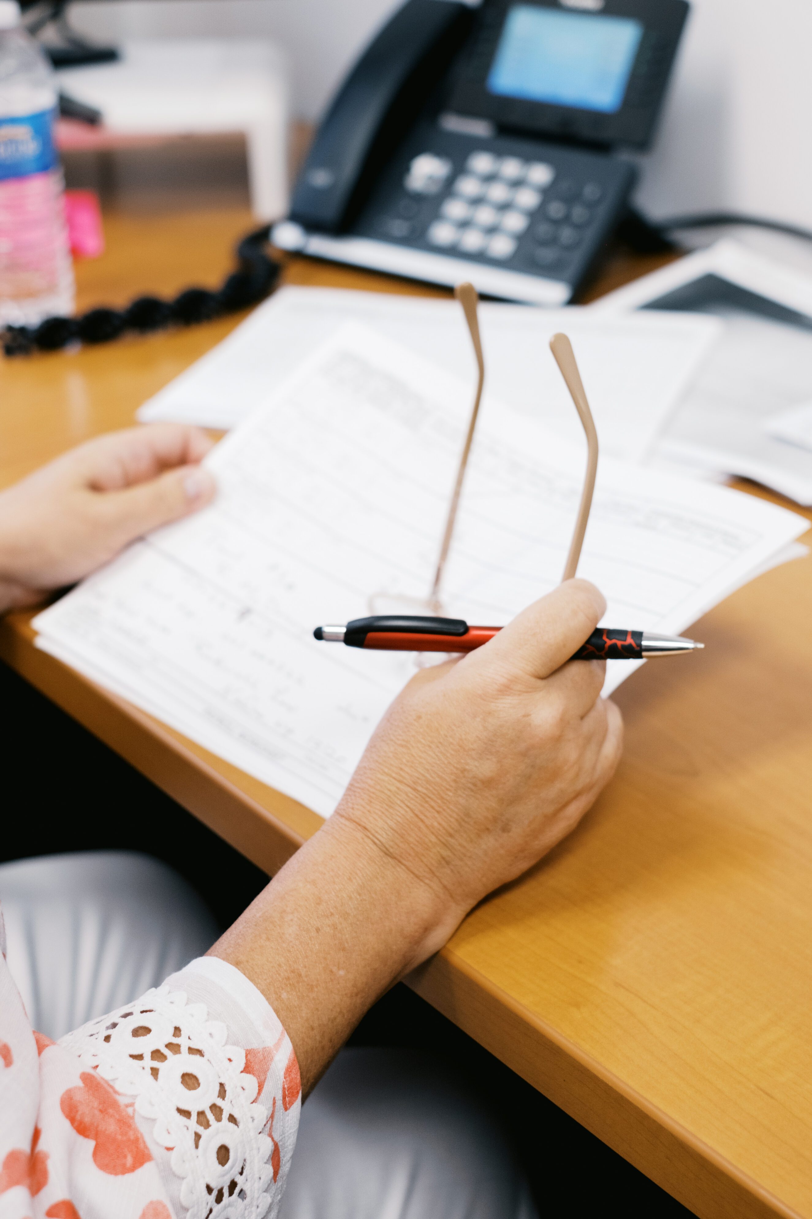 Person reviewing payroll documents at a desk with a pen and glasses in hand, next to a telephone, representing personalized payroll solutions and business-focused payroll management.